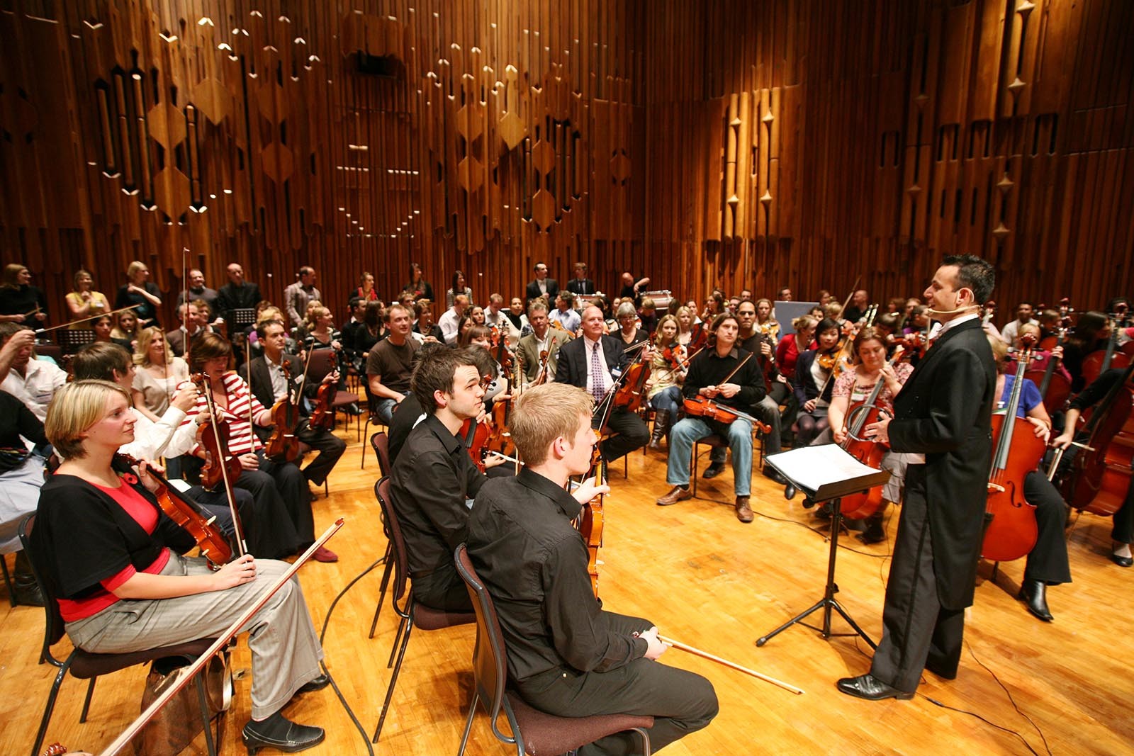 Hudebni dirigent vysvetluje ucastnikum jaka prace je za sestavenim orchestru pri hre Orchestrate